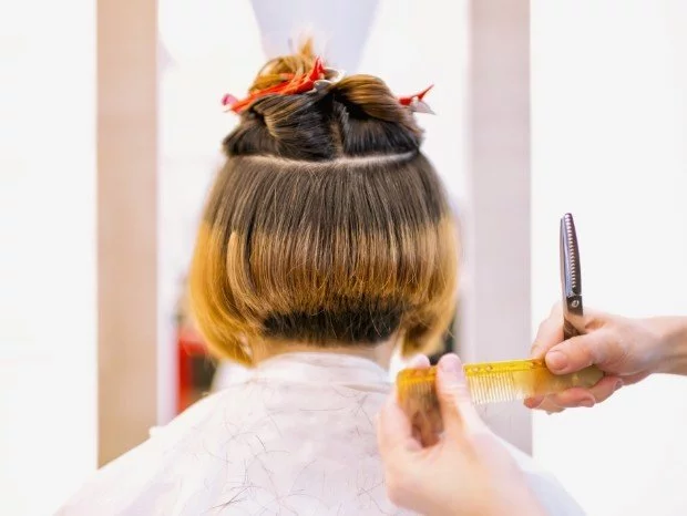 Grzebień i nożyczki w dłoniach fryzjera obok klientki